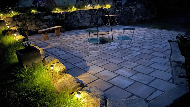 A paved patio with stone walls, a wooden bench, a metal table, and chairs.