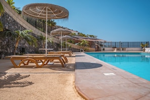 Uma área à beira da piscina com espreguiçadeiras, guarda-sóis e vista direta para a piscina.