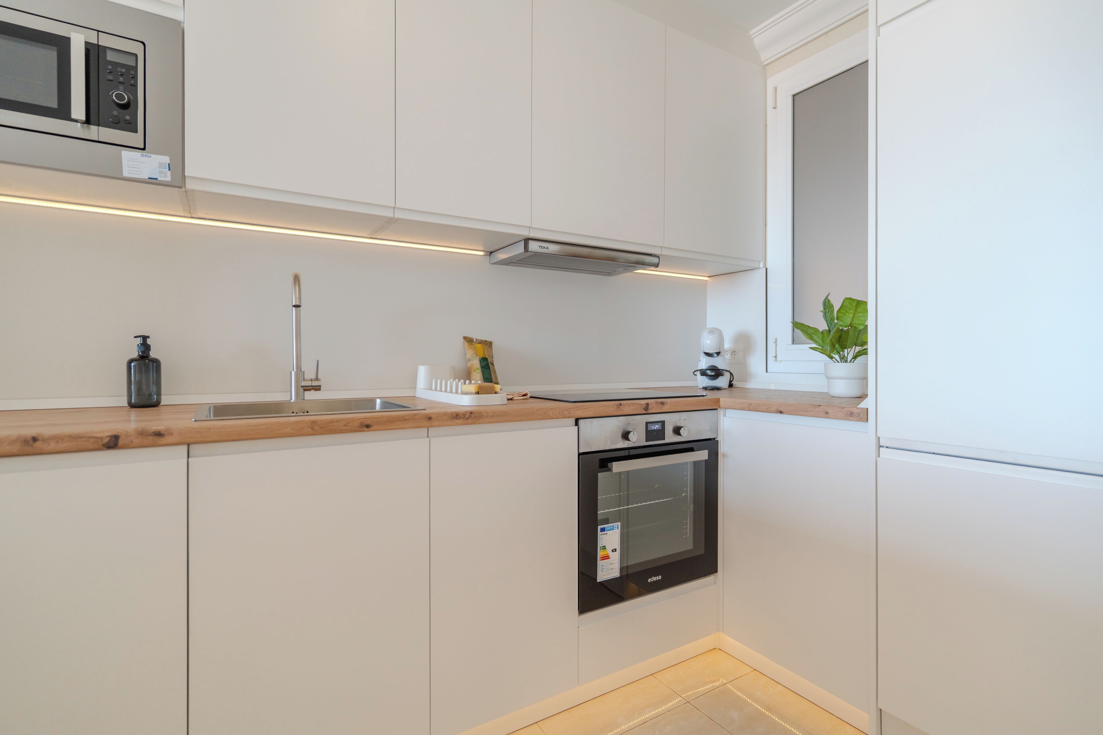 A modern kitchen with white cabinets, a built-in oven, a microwave, and a wooden countertop.