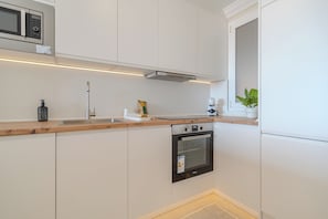 Cozinha moderna com armários brancos, forno embutido, micro-ondas e bancada de madeira.
