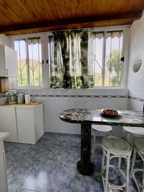 Cozinha com mesa de mármore, armários brancos e vista pela janela.