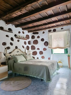 Ein Schlafzimmer mit einem Bett, einem Nachttisch, einer Lampe, einem Fenster mit Vorhang und einer Wand mit kreisrunden Öffnungen.