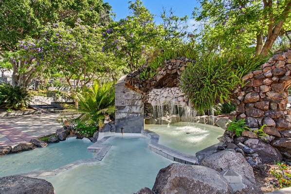 A stone water feature with a small waterfall, surrounded by lush greenery and trees.