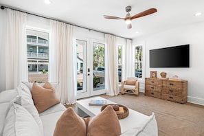 A modern living room with a sofa, a coffee table, a wicker side table, a ceiling fan, and a TV mounted on the wall. - NEW LISTING - Completely remodeled with new pics coming soon. (Seacrest Beach)
