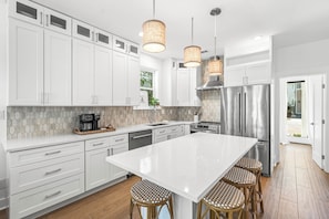 Una cocina moderna con armarios blancos, electrodomésticos de acero inoxidable, una isla grande con taburetes e iluminación colgante.