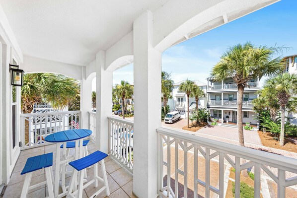 Een balkon met witte reling, een blauwe tafel en twee blauwe stoelen.