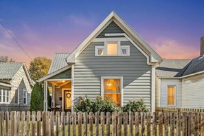 A two-story house with a front porch, a visible garage door, and a wooden fence. - Stylish Indy Retreat in a Great Location (Indianapolis)