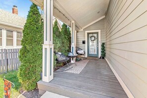 A covered porch with a wooden deck, a door with a wreath, and two chairs. - Stylish Indy Retreat in a Great Location (Indianapolis)
