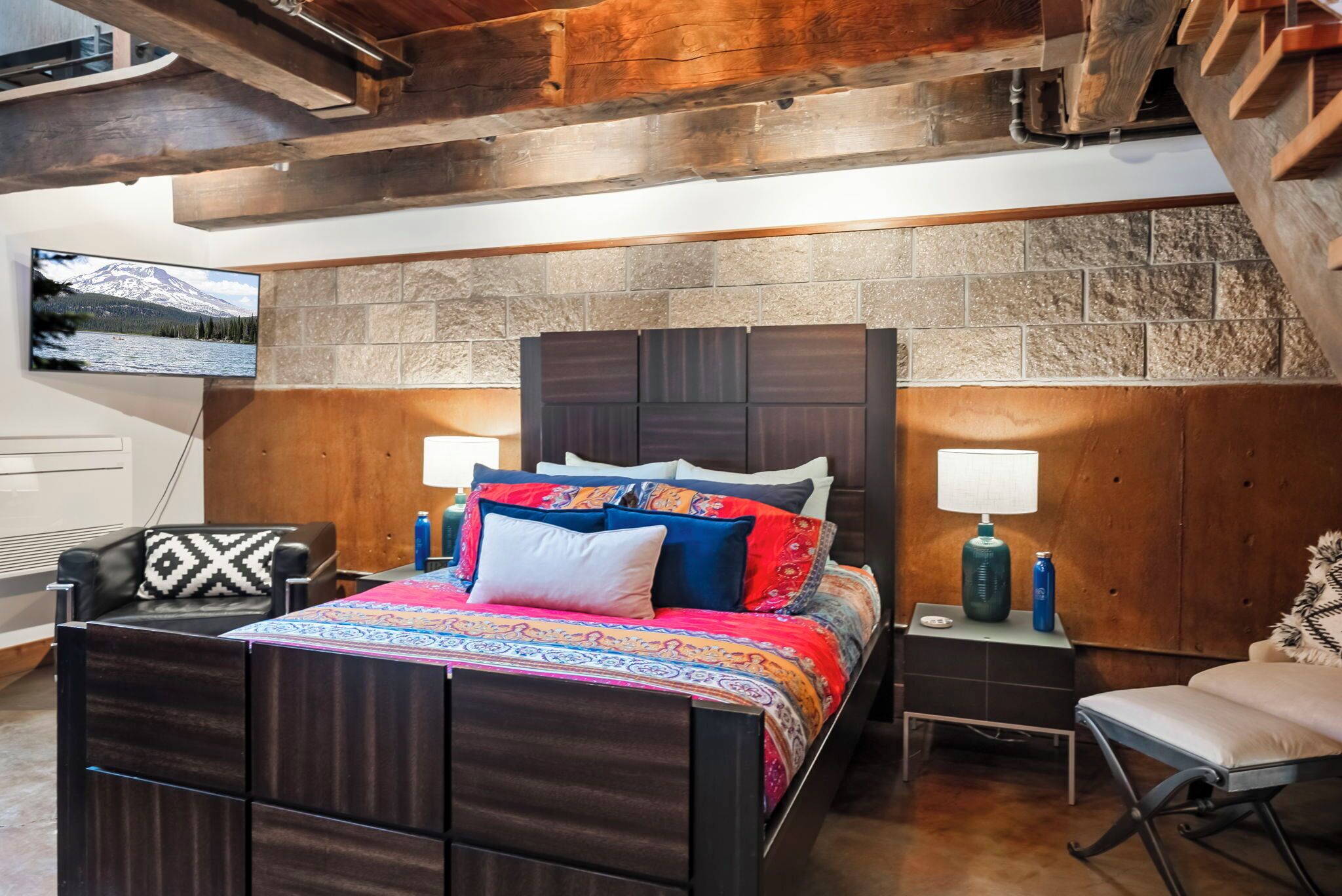 Un dormitorio con una cama grande, dos mesitas de noche, un televisor montado y una pared de piedra.