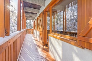 Ein hölzerner Balkon mit schneebedeckten Geländern und Blick auf einen verschneiten Wald.