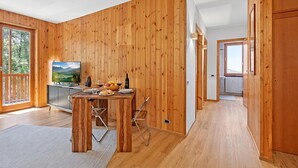 A wooden-paneled room with a dining table, chairs, a TV, and a kitchen area. - L'anemone Near Campo Smith Lifts (Bardonecchia)