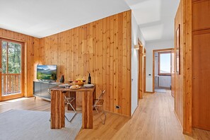 A wooden-paneled room with a dining table, chairs, a TV, and a kitchen area. - L'anemone Near Campo Smith Lifts (Bardonecchia)