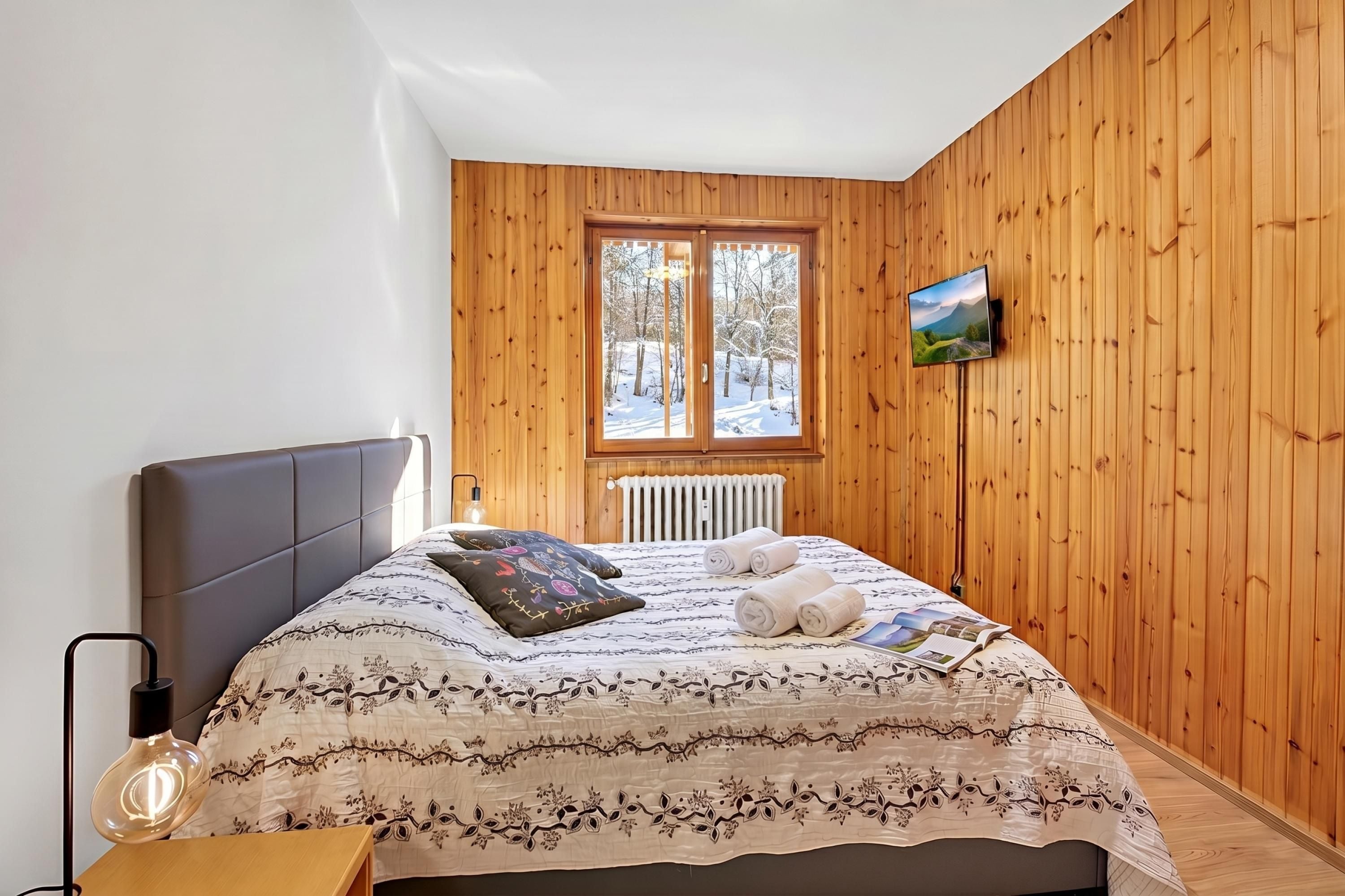 Un dormitorio con cama, ventana, radiador y televisor.