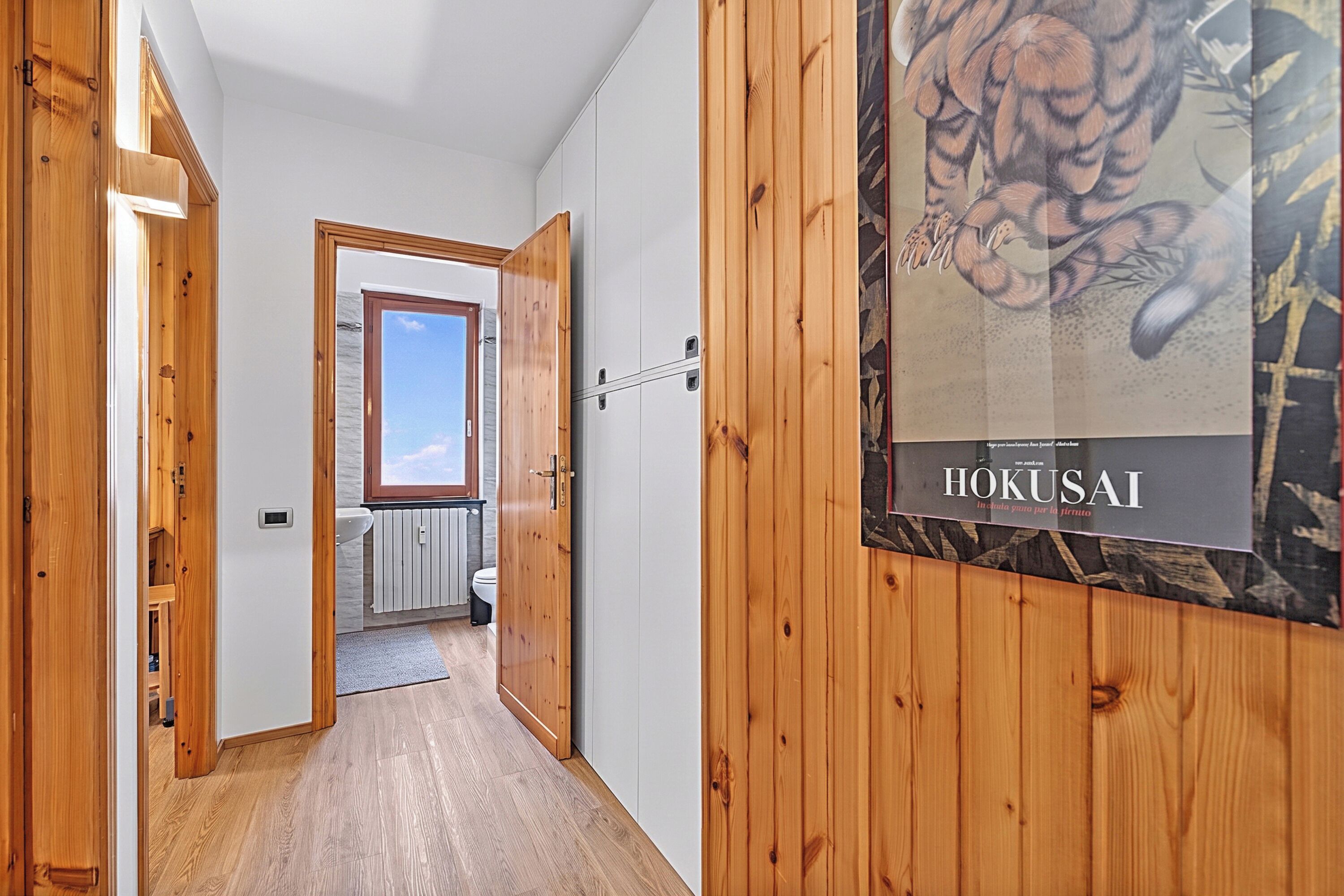 Un couloir aux murs en bois, avec un radiateur, une fenêtre et une porte donnant sur une salle de bain.