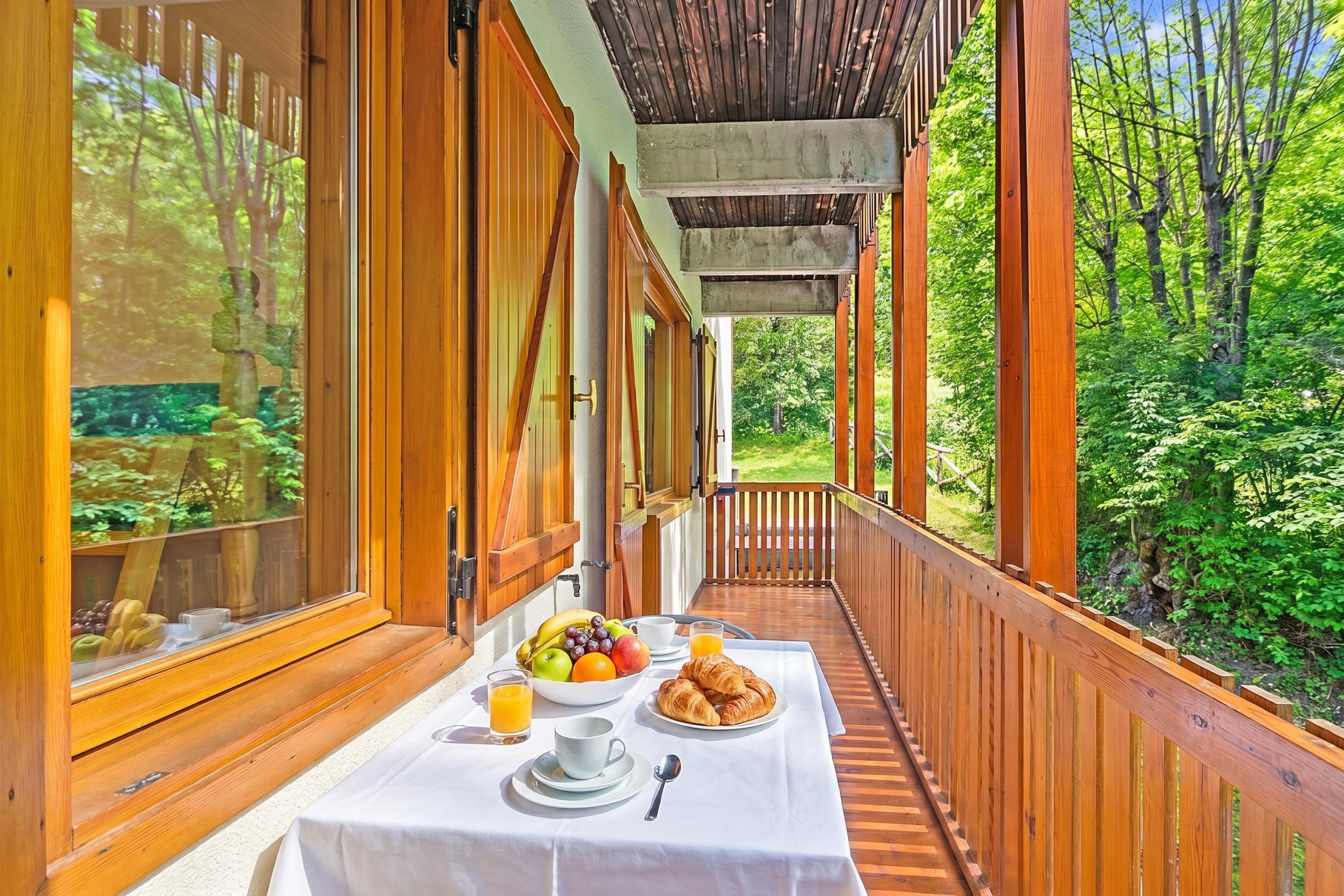 A wooden deck with a table set for breakfast, including fruits, croissants, and juice.