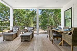 Een overdekt terras met rieten meubilair, een eettafel en uitzicht op bomen.