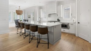 Una cocina moderna con una isla grande, taburetes de bar y un comedor con candelabro.