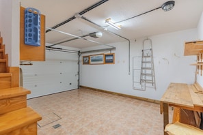 A garage with a wooden staircase, a white garage door, a ceiling with exposed pipes and lights, and a ladder against the wall. - Conde Sunset View (Costa Adeje)