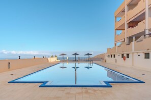 A swimming pool with a clear view of the sea, a building with balconies, and a tiled deck. - Conde Sunset View (Costa Adeje)