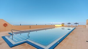 Ein rechteckiger Swimmingpool mit glasklarer, blauer Wasseroberfläche, umgeben von einer gefliesten Terrasse.