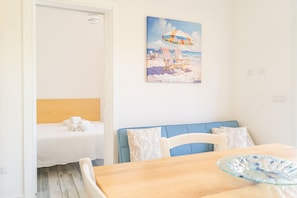 A room with a bed, a table with a glass bowl, a painting of a beach scene, and a blue chair. - Domo de Mare - Two Bedroom Apartment, Sleeps 5 (Iscra E Voes)