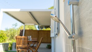 Un rociador de ducha en la pared, una silla de madera y una mesa en un área exterior cubierta.