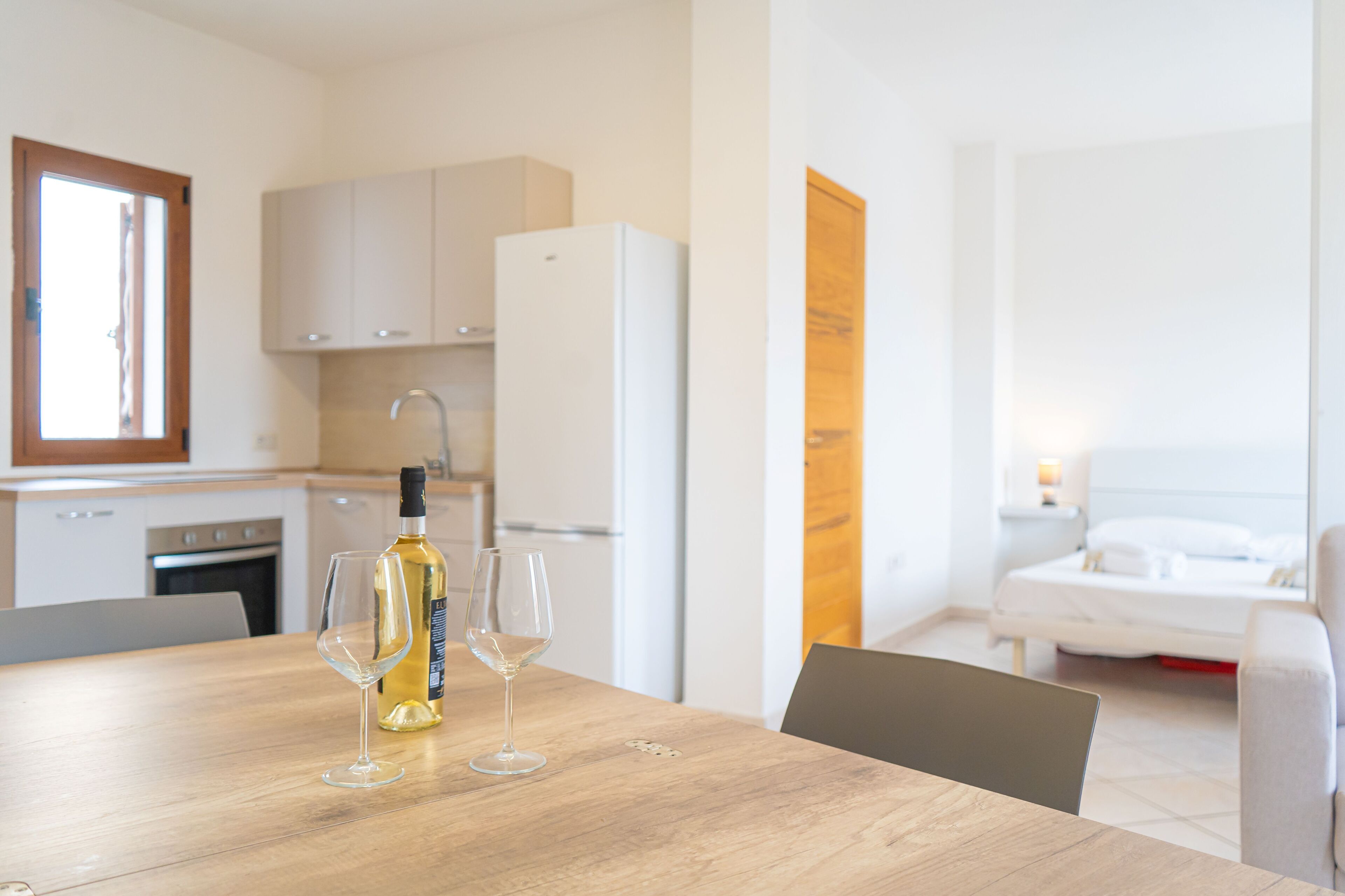 Een moderne keuken met witte kasten, een koelkast en een eettafel met een fles wijn en glazen.