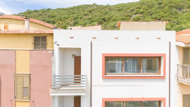 Un edificio con balcón, una ventana de marco rosa y una puerta.