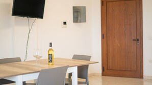 Un comedor con una mesa, sillas, una botella de vino y un televisor montado en la pared.