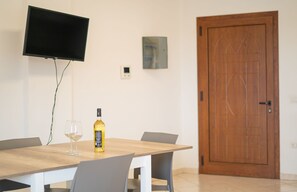 Ein Essbereich mit Tisch, Stühlen, einer Weinflasche und einem an der Wand befestigten Fernseher.