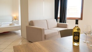 Una habitación de hotel moderna con un sofá, una mesa de madera, una botella de vino Elive y dos copas.