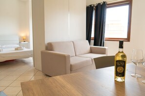 Ein modernes Hotelzimmer mit einer Sitzecke, einem Holztisch, einer Flasche Elive Wein und zwei Gläsern.