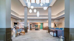 Un'ampia hall con zona salotto centrale, una reception e, sullo sfondo, un negozio chiamato 'The Shop'.
