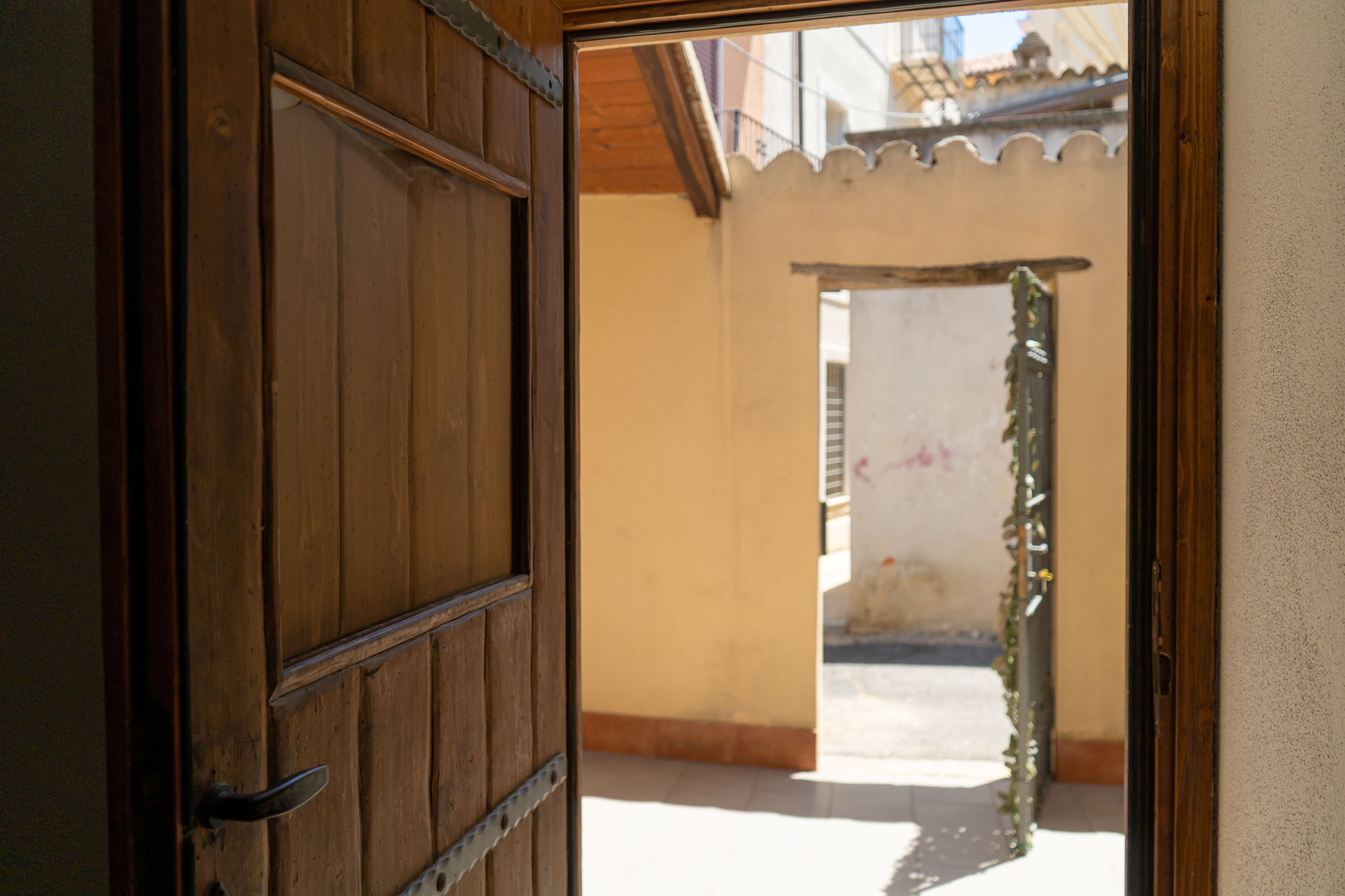 Uma porta de madeira aberta dá para um corredor com piso ladrilhado e um painel decorativo na parede.