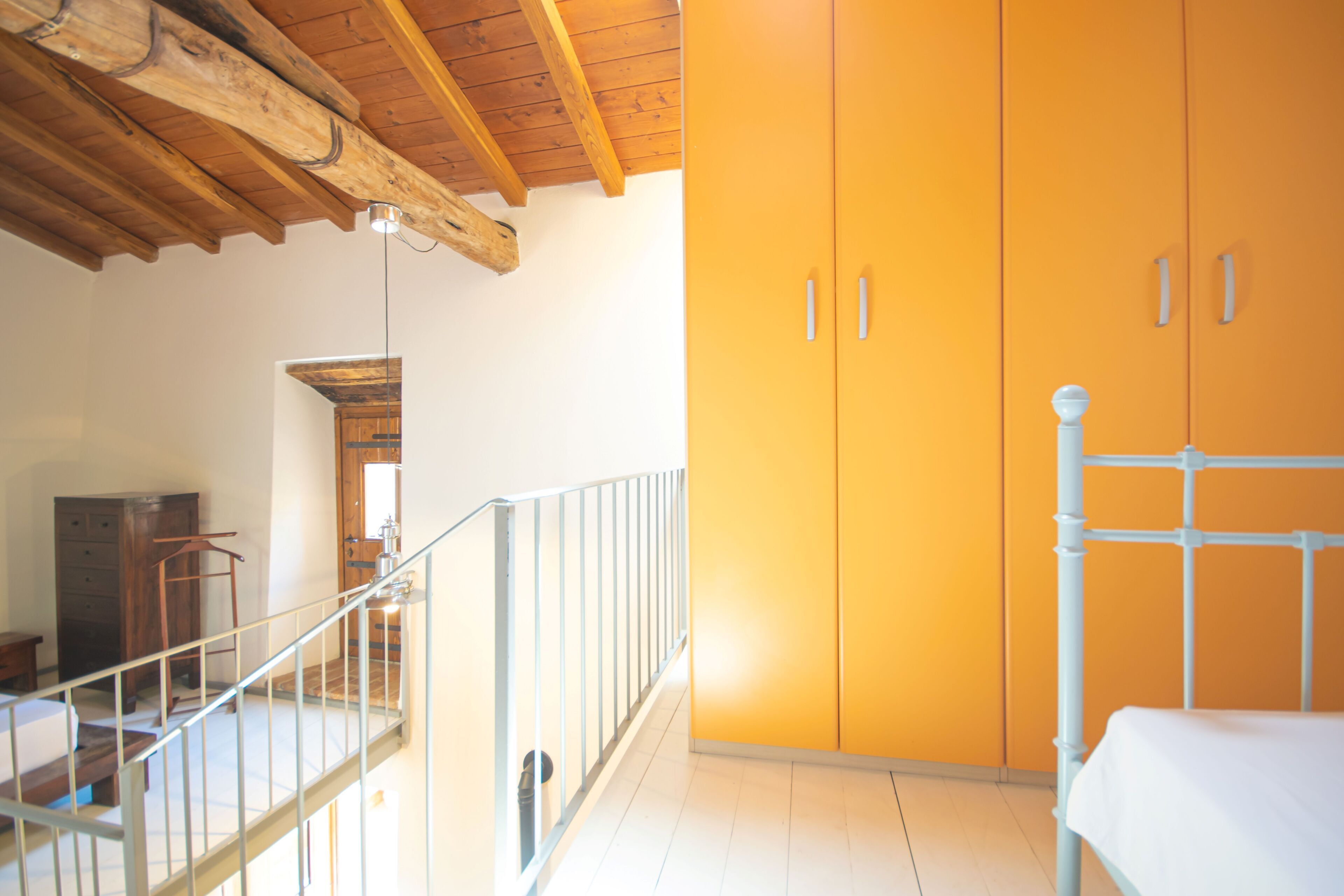 Een kamer met een houten plafond, een trap, een bed en een kledingkast.