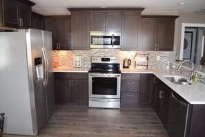 A modern kitchen with dark cabinets, stainless steel appliances, a microwave, oven, and a sink. - City Park Retreat | Near Golf, Parks & Old Town (Fort Collins)