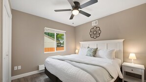 A bedroom with a bed, nightstands, a ceiling fan, a window, and a wall decoration.