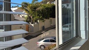 Ein Fenster mit Jalousien, Blick auf eine Straße, ein geparktes Auto und ein Gebäude mit Garage.