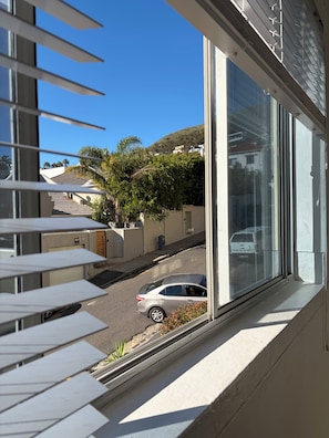 Ein Fenster mit Jalousien, Blick auf eine Straße, ein geparktes Auto und ein Gebäude mit Garage.