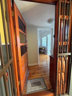 A wooden door with a glass panel, a doormat, and a hallway leading to a dining area with a table and chairs. - 2 bedroom newly refurnished apartment in Green Point (Cape Town)
