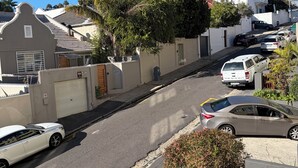 Eine Wohnstraße mit geparkten Autos, einem verschlossenen Eingang und Häusern mit roten Dächern.