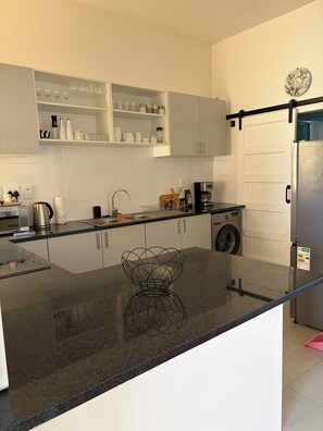 A modern kitchen with a granite countertop, a built-in oven, a coffee maker, and a washing machine. - 2 bedroom newly refurnished apartment in Green Point (Cape Town)