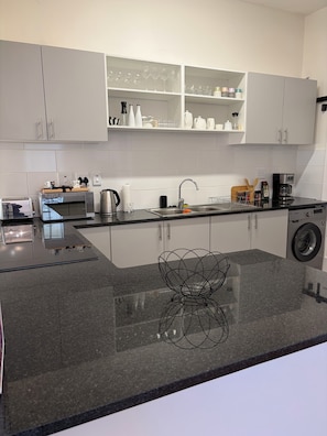 Eine moderne Küche mit weißen Schränken, einer Granitarbeitsplatte, einer Kaffeemaschine, einer Mikrowelle und einer Waschmaschine.