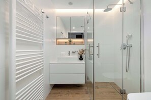 A modern bathroom with a glass shower enclosure, a white vanity with a mirror, and a wooden floor. - Cozy Studios Near the Beach | Parking (Pobierowo)