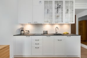 A modern kitchen with white cabinetry, a black countertop, a coffee maker, a sink, and a fruit bowl. - Cozy Studios Near the Beach | Parking (Pobierowo)