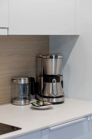 Een keuken met een koffiezetapparaat, een glazen kan en een bord met koffiecups.