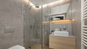 Un baño moderno con ducha envuelta en vidrio, un lavabo blanco y un mueble de tocador de madera.