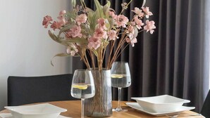 Una mesa redonda de comedor con un jarrón de flores rosadas, dos copas de vino y platos blancos.