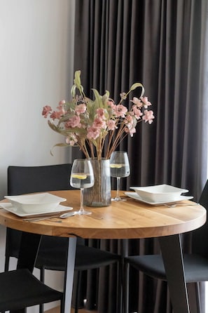 A round dining table with a vase of pink flowers, two wine glasses, and white plates. - Cozy Studios Near the Beach | Parking (Pobierowo)