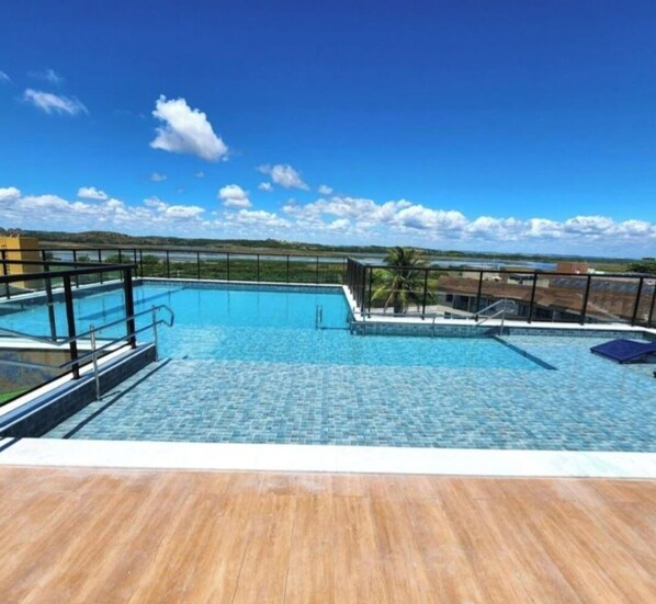 A rooftop swimming pool with clear blue water, surrounded by a wooden deck and a metal railing. - Porto Atlantis 308, just steps from the ocean in Porto de Galinhas (Ipojuca)